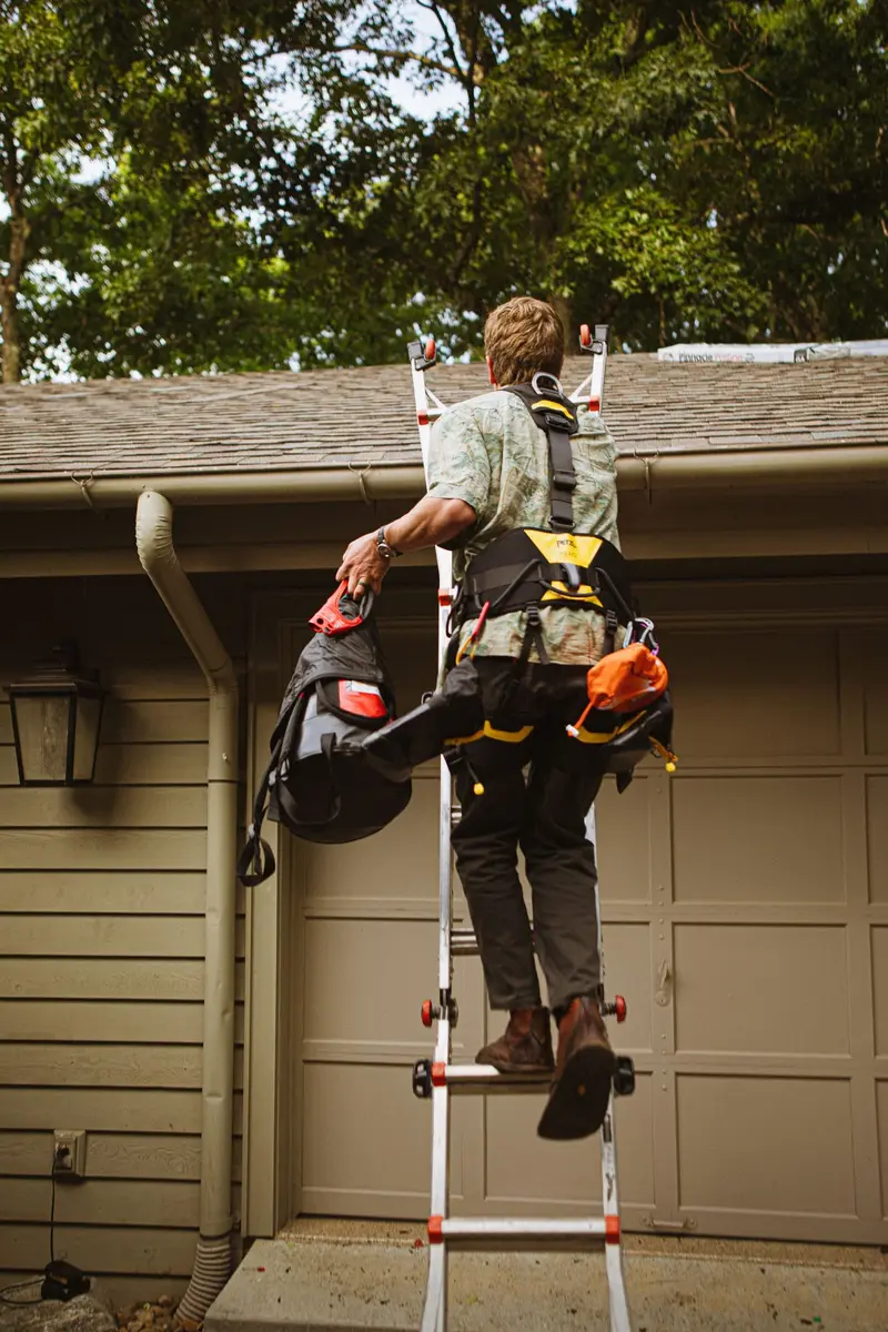 Worker in a safety harness climbing a ladder to the gutter line of a house